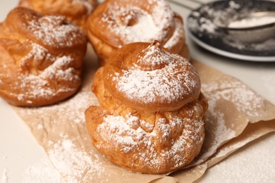 Delicious profiteroles with powdered sugar on parchment paper, closeup