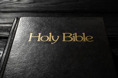 Photo of Bible with dark cover on black wooden table, closeup. Christian religious book