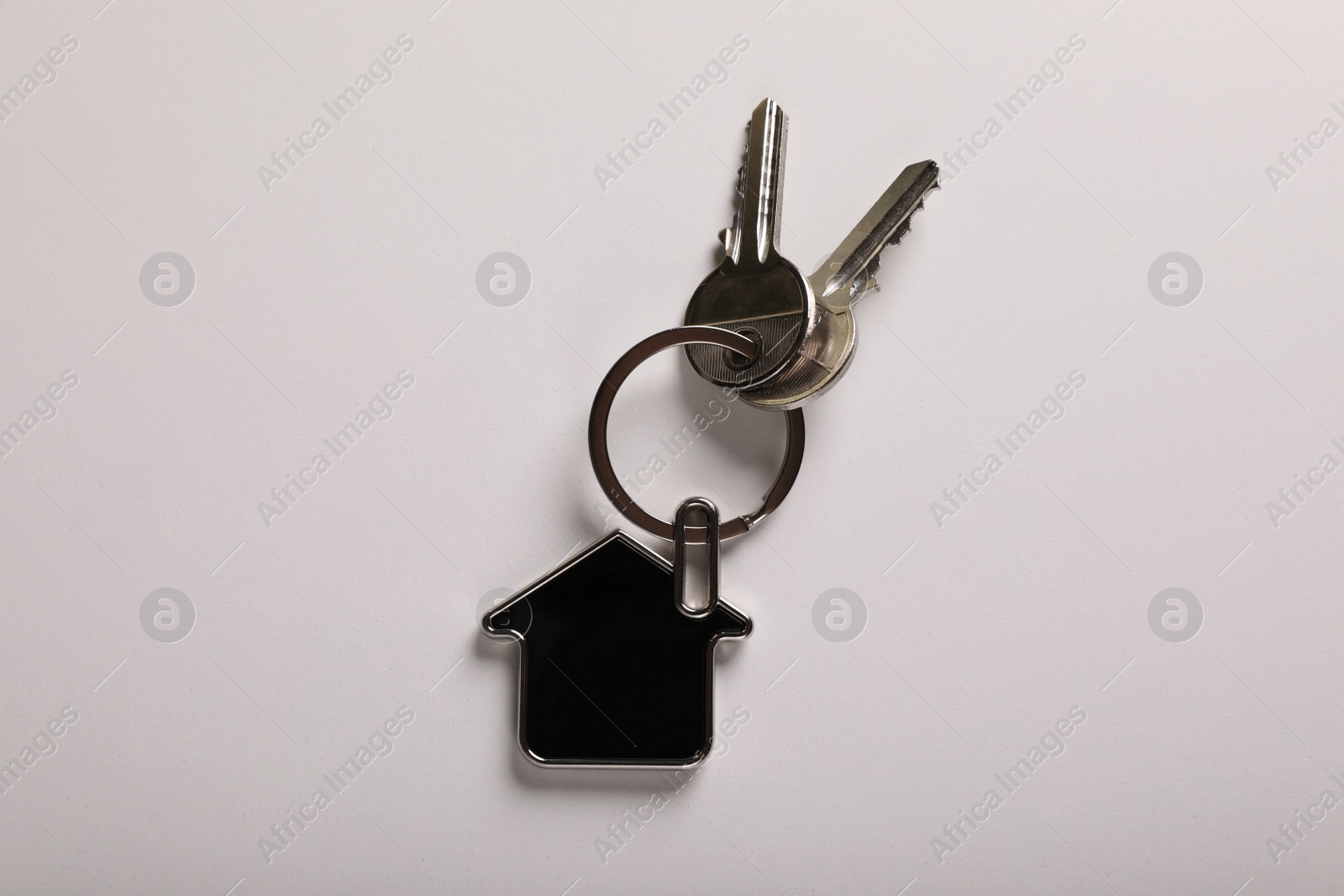 Photo of Keys with trinket in shape of house on white background, top view. Real estate agent services