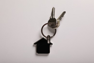 Keys with trinket in shape of house on white background, top view. Real estate agent services