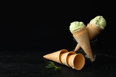 Photo of Delicious pistachio ice cream in wafer cones served on black table. Space for text