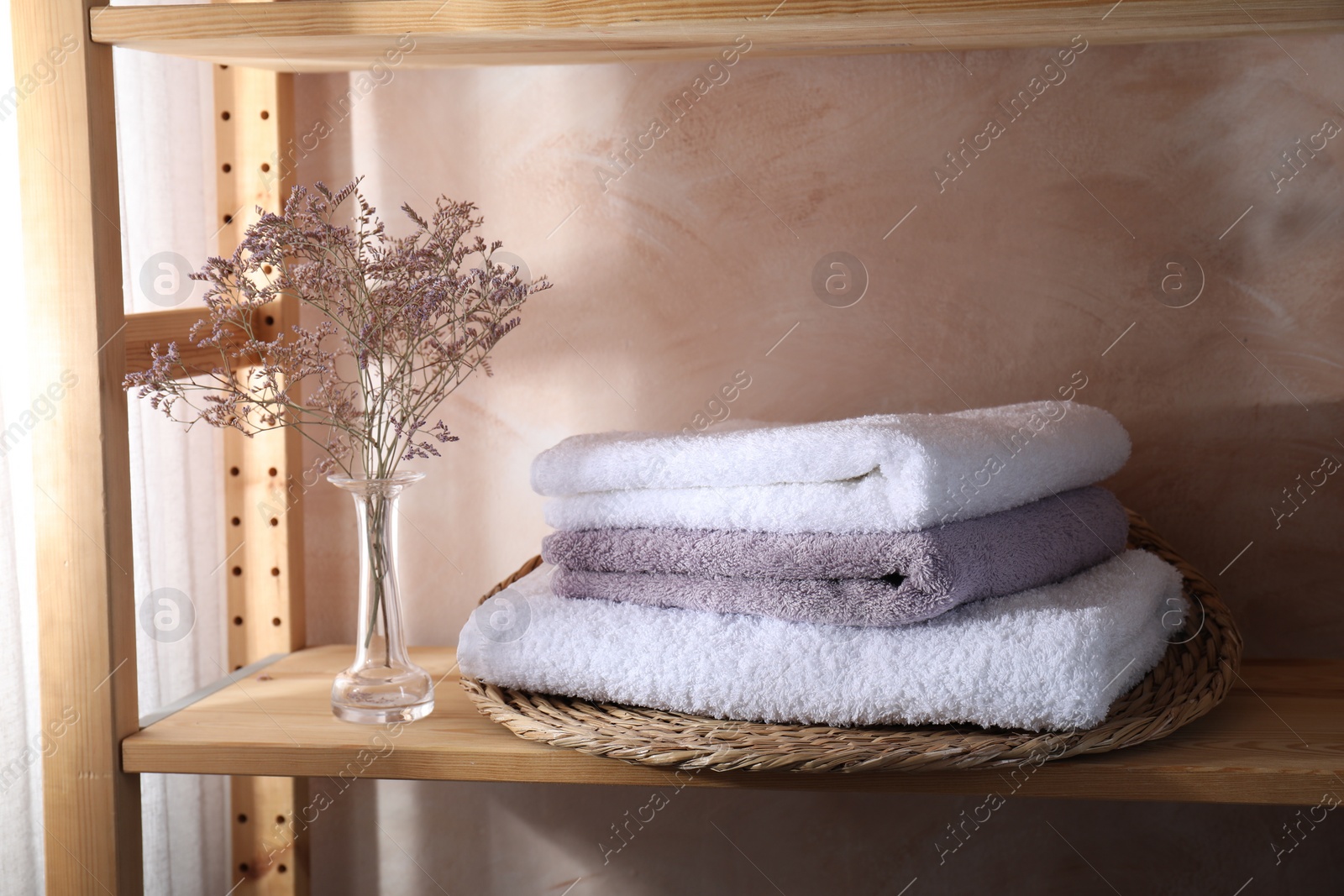 Photo of Stacked soft towels and flowers on wooden shelf indoors