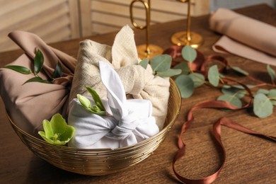 Photo of Furoshiki technique. Gifts packed in different fabrics and flowers on wooden table, closeup. Space for text