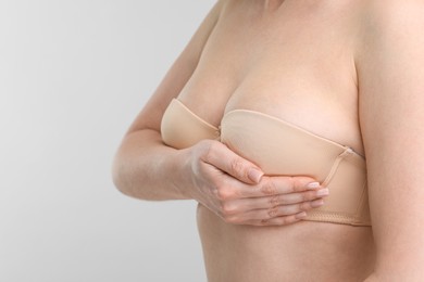 Mammology. Young woman doing breast self-examination on light grey background, closeup