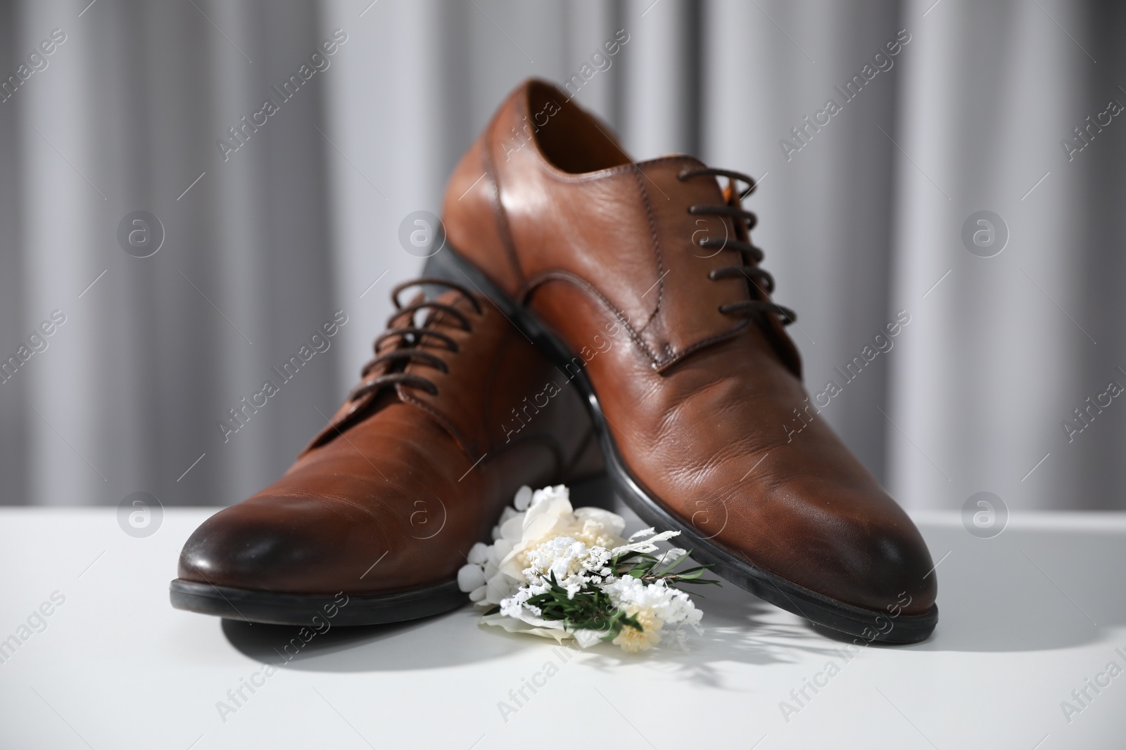 Photo of Wedding stuff. Stylish boutonniere and brown shoes on white surface against gray background, closeup