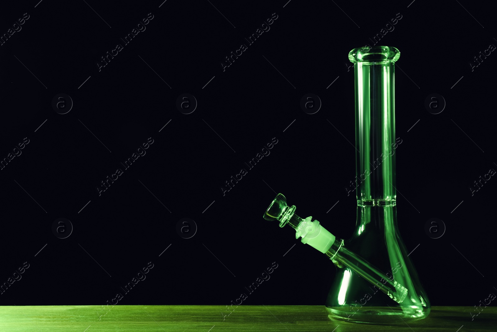 Photo of Glass bong on wooden table against black background, space for text. Smoking device