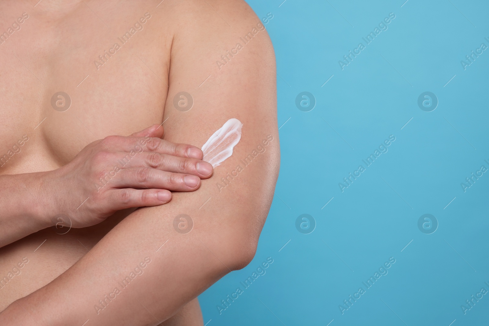 Photo of Man applying body cream onto his arm on light blue background, closeup. Space for text