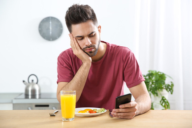 Photo of Young man addicted to smartphone having breakfast at home