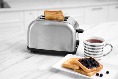 Modern toaster and tasty breakfast on white marble table in kitchen