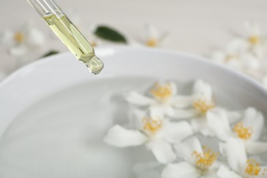 Photo of Dripping jasmine essential oil into bowl with flowers, closeup