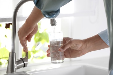 Photo of Man pouring water into glass in kitchen, closeup