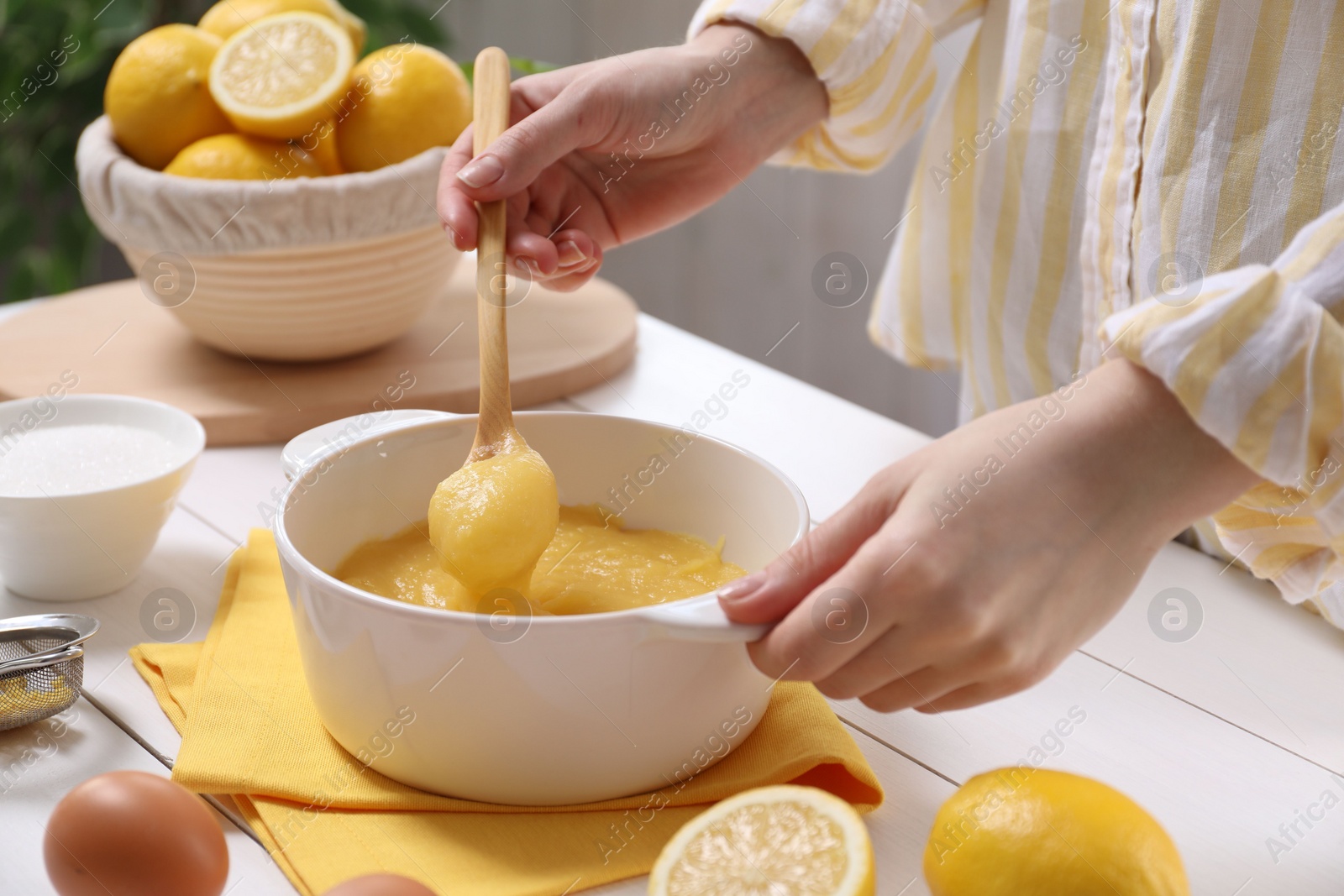 Photo of Woman cooking lemon curd at white wooden table, closeup