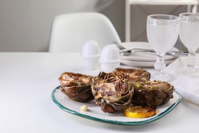 Photo of Plate with tasty grilled artichokes served on white table. Space for text