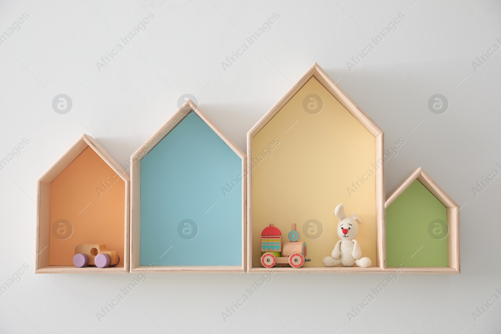 Photo of Different house shaped shelves with toys on white wall. Interior design