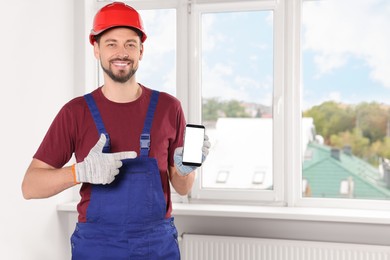 Professional repairman in uniform with phone indoors, space for text