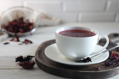 Photo of Delicious hibiscus tea in cup and dry roselle petals on white wooden table, closeup. Space for text
