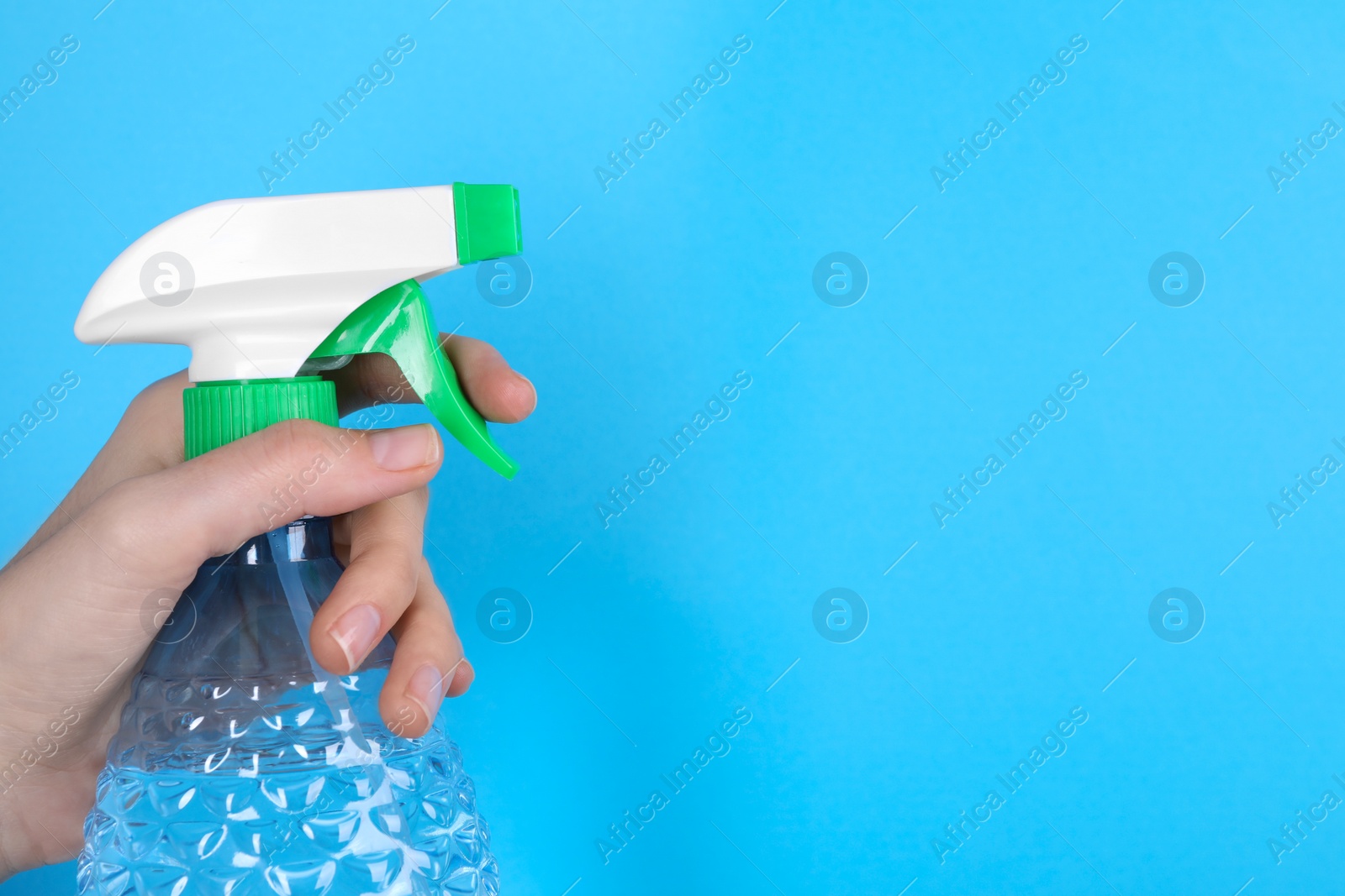 Photo of Woman holding plastic spray bottle on light blue background, closeup. Space for text