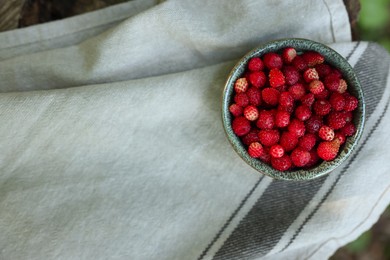 Photo of Bowl of tasty wild strawberries on cloth, top view. Space for text