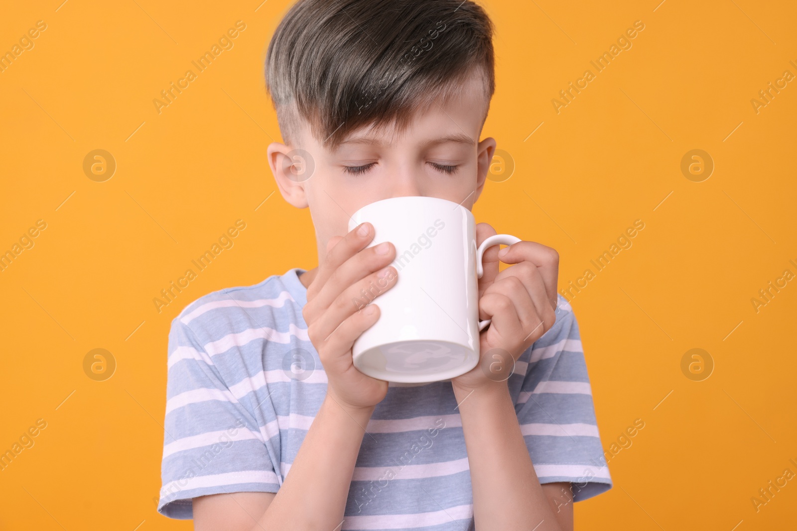Photo of Cute boy drinking beverage from white ceramic mug on orange background