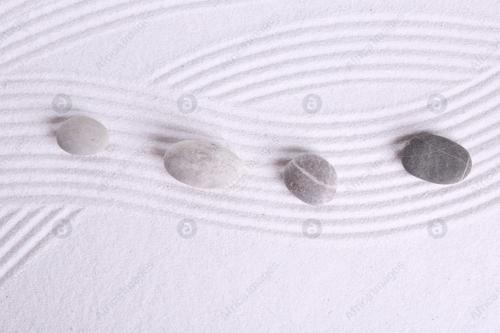 Photo of Zen garden stones on white sand with pattern, flat lay