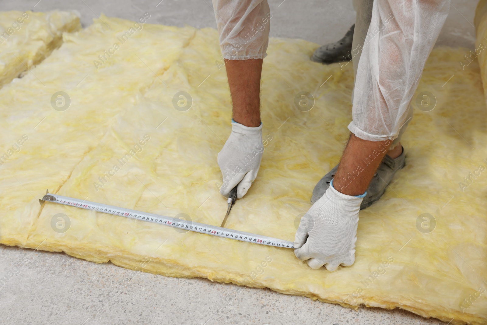 Photo of Worker measuring and cutting insulation material indoors, closeup