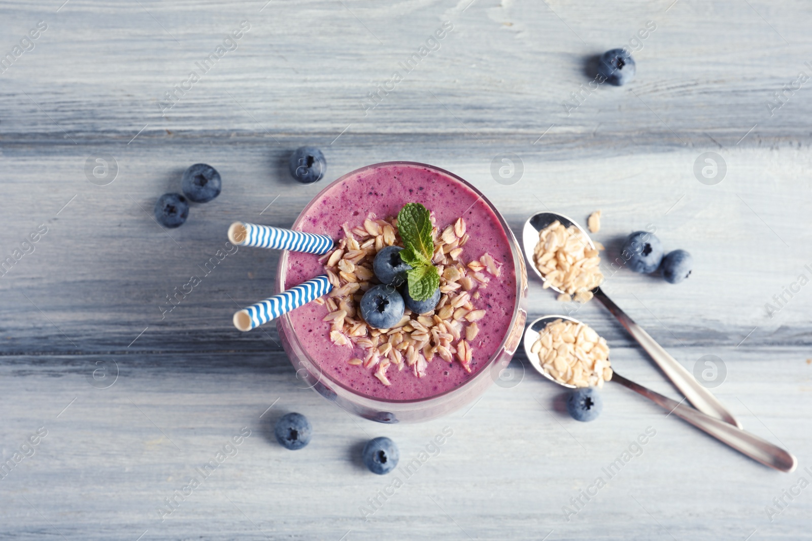 Photo of Tasty blueberry smoothie in glass, berries and oatmeal on wooden table, top view