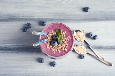 Tasty blueberry smoothie in glass, berries and oatmeal on wooden table, top view