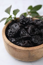 Sweet dried prunes in bowl on white table, closeup