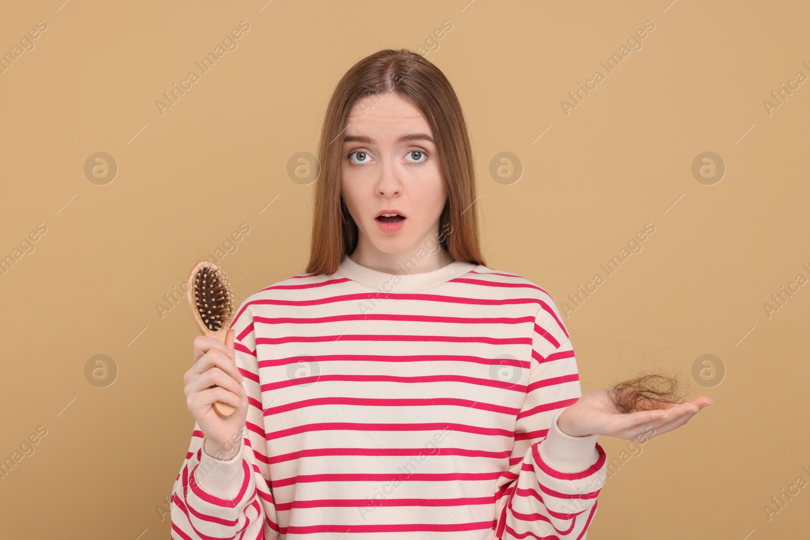 Photo of Emotional woman holding brush with lost hair on beige background. Alopecia problem