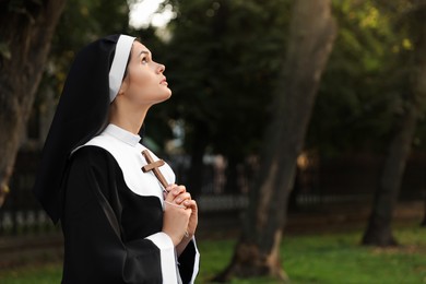 Photo of Young nun with Christian cross in park outdoors, space for text