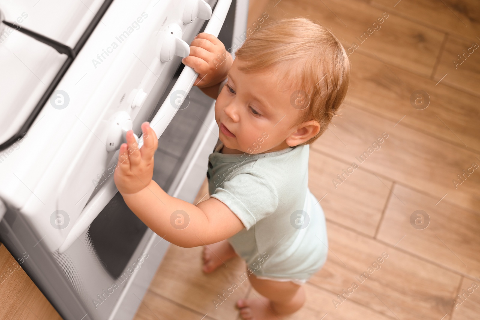 Photo of Little child playing with gas stove indoors, above view. Dangers in kitchen