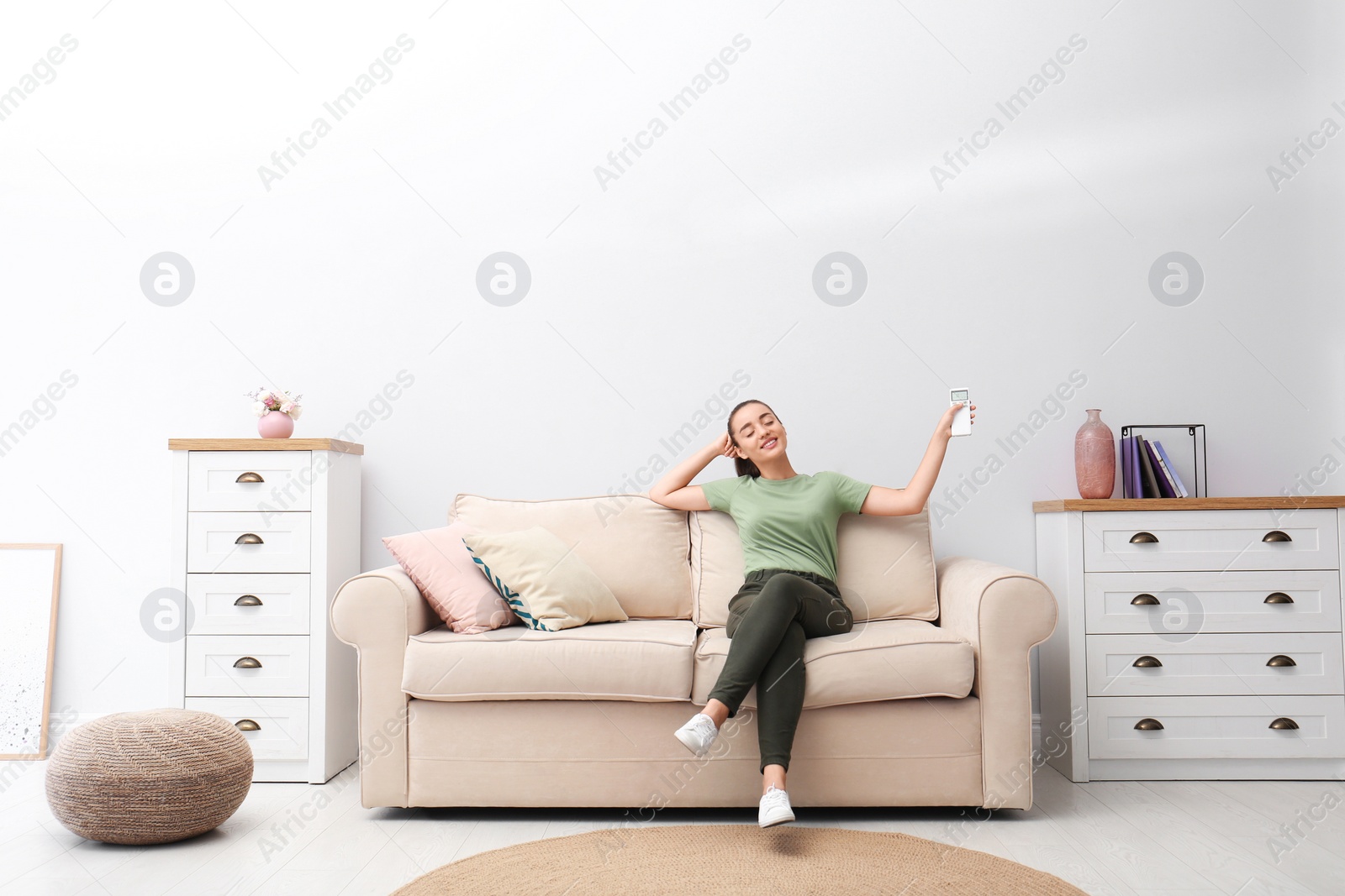 Photo of Happy young woman switching on air conditioner with remote control at home