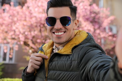 Photo of Happy man with sunglasses taking selfie outdoors on spring day
