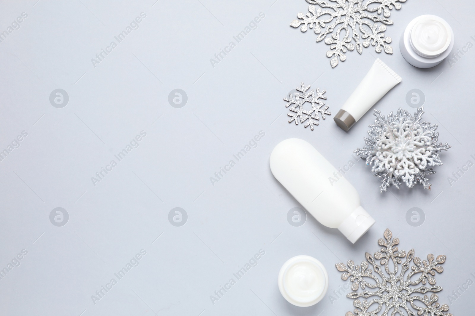 Photo of Flat lay composition with cosmetic products and snowflakes on light grey background, space for text. Winter skin care