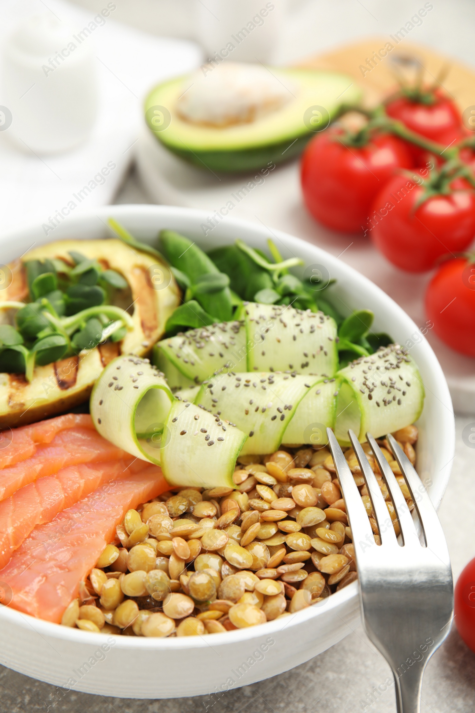 Photo of Delicious lentil bowl with salmon, avocado and cucumber on grey table