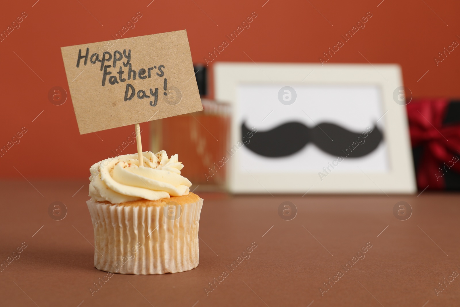 Photo of Happy Father's Day. Tasty cupcake with greetings on brown table, closeup. Space for text