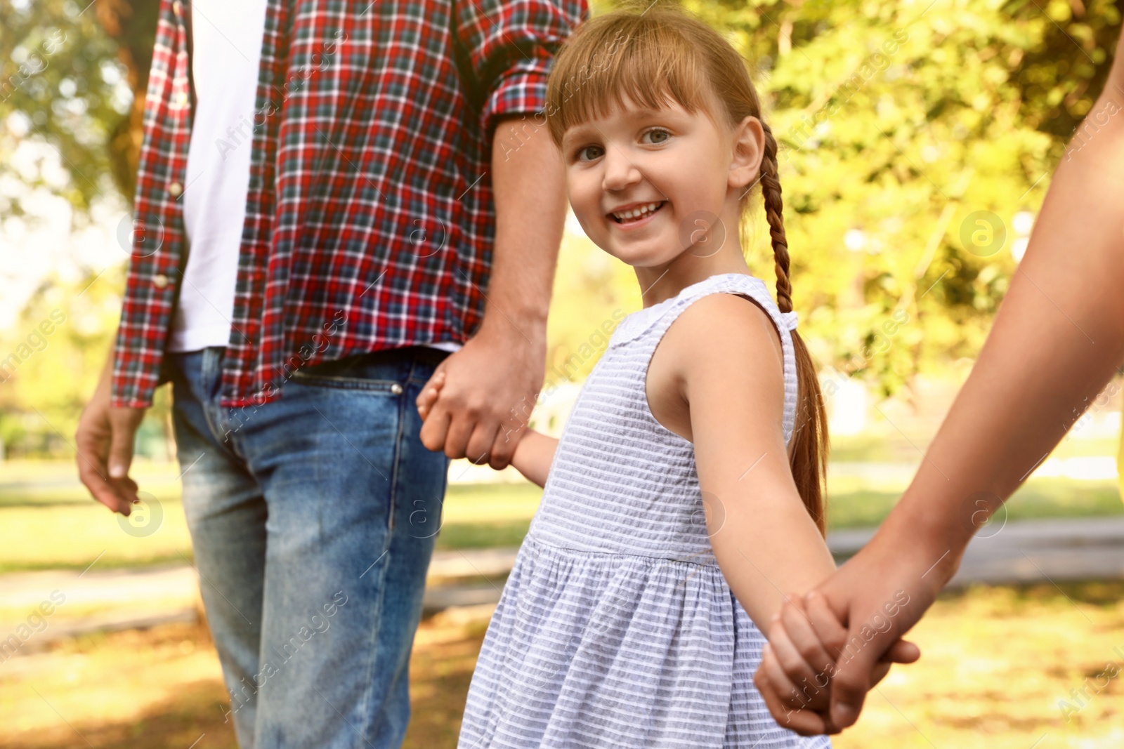 Photo of Little girl and her parents holding hands outdoors. Family weekend