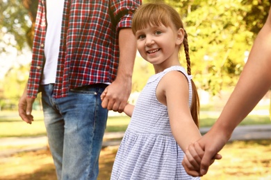 Little girl and her parents holding hands outdoors. Family weekend