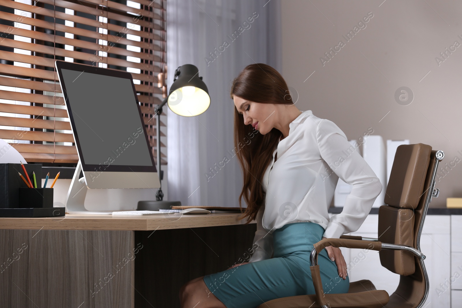 Photo of Young woman suffering from hemorrhoid at workplace in office