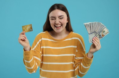 Happy woman with credit card and dollar banknotes on light blue background