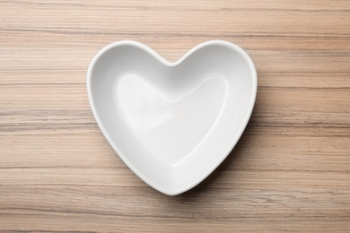 Heart shaped plate on wooden background, top view