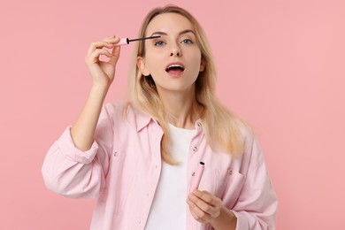 Photo of Beautiful woman applying mascara on pink background