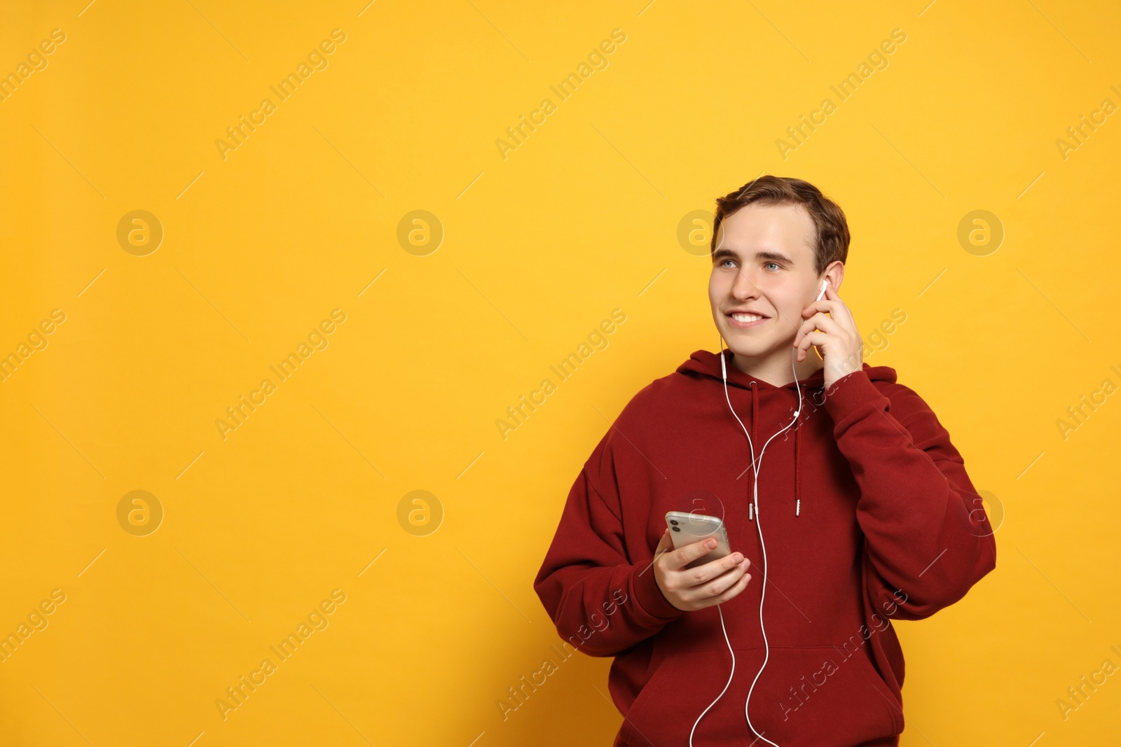 Photo of Handsome young man with earphones and smartphone on yellow background. Space for text