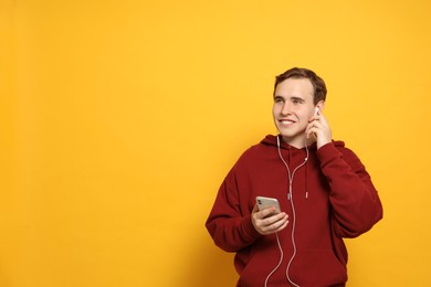 Handsome young man with earphones and smartphone on yellow background. Space for text