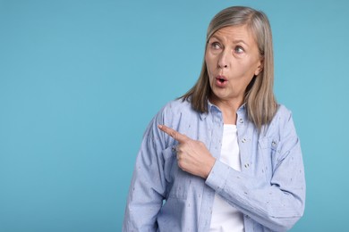 Photo of Surprised senior woman pointing at something on light blue background, space for text