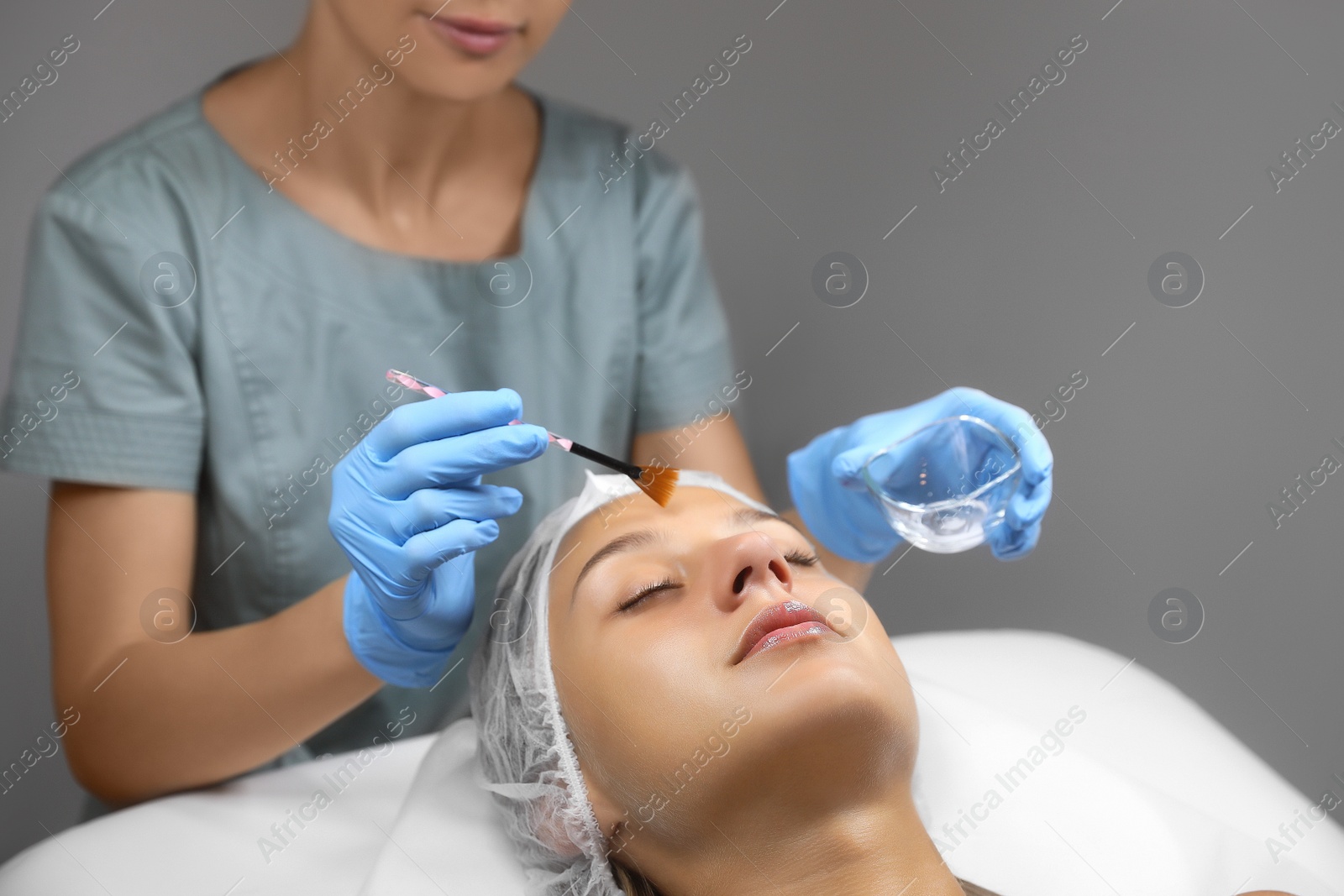 Photo of Cosmetologist applying cosmetic product for chemical peeling on client's face in salon