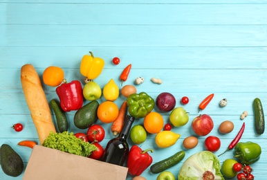 Flat lay composition with overturned paper bag and groceries on blue wooden background