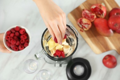 Photo of Woman adding raspberry into blender with ingredients for smoothie at table, top view