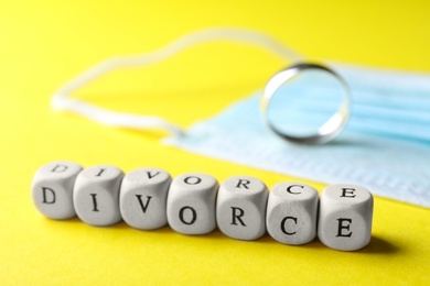 Cubes with word Divorce, protective mask and wedding ring on yellow background, closeup