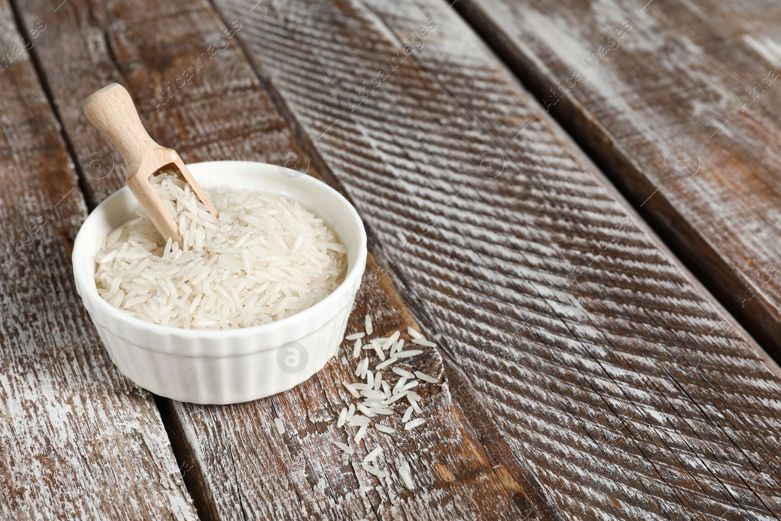 Photo of Raw basmati rice in bowl and scoop on wooden table, space for text